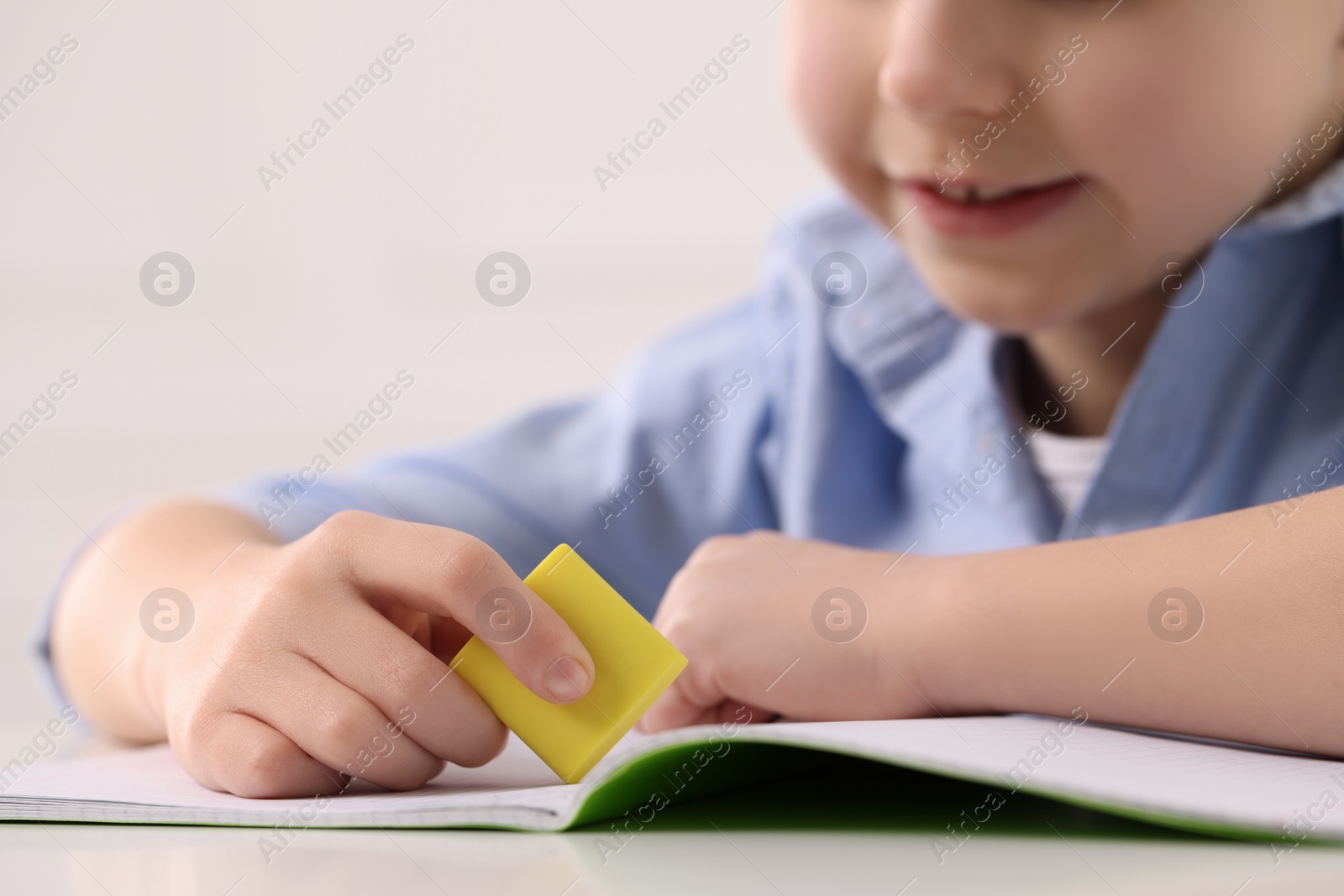 Photo of Little boy erasing mistake in his notebook at white desk, closeup