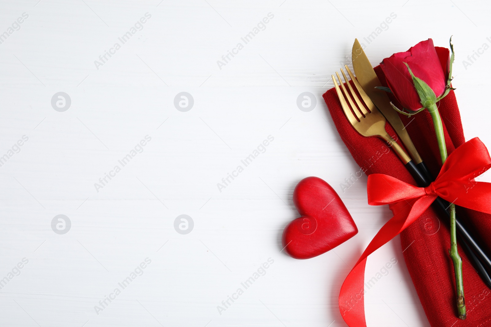 Photo of Top view of cutlery with napkin and decorative heart on white wooden table, space for text. Valentine's Day romantic dinner