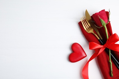 Top view of cutlery with napkin and decorative heart on white wooden table, space for text. Valentine's Day romantic dinner