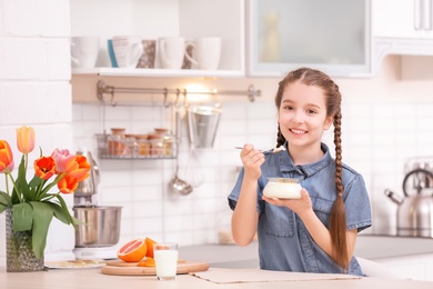 Photo of Cute girl eating tasty yogurt at table in kitchen