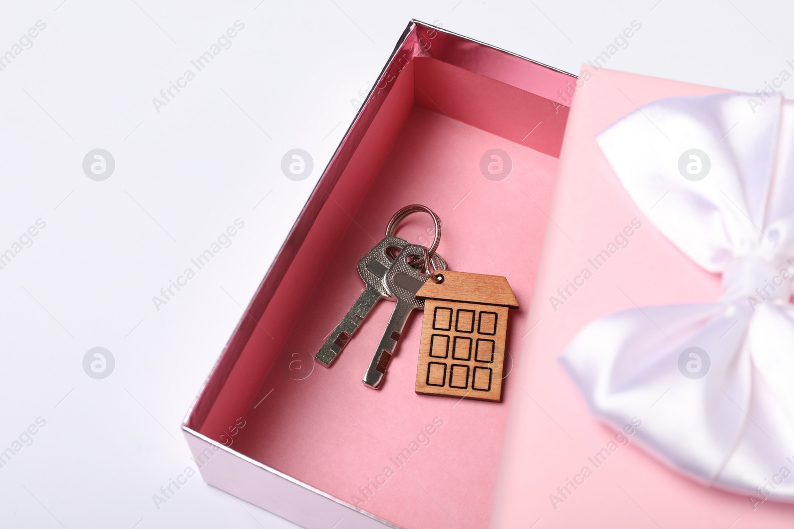 Photo of Keys with trinket in shape of house and gift box on white background. Housewarming party