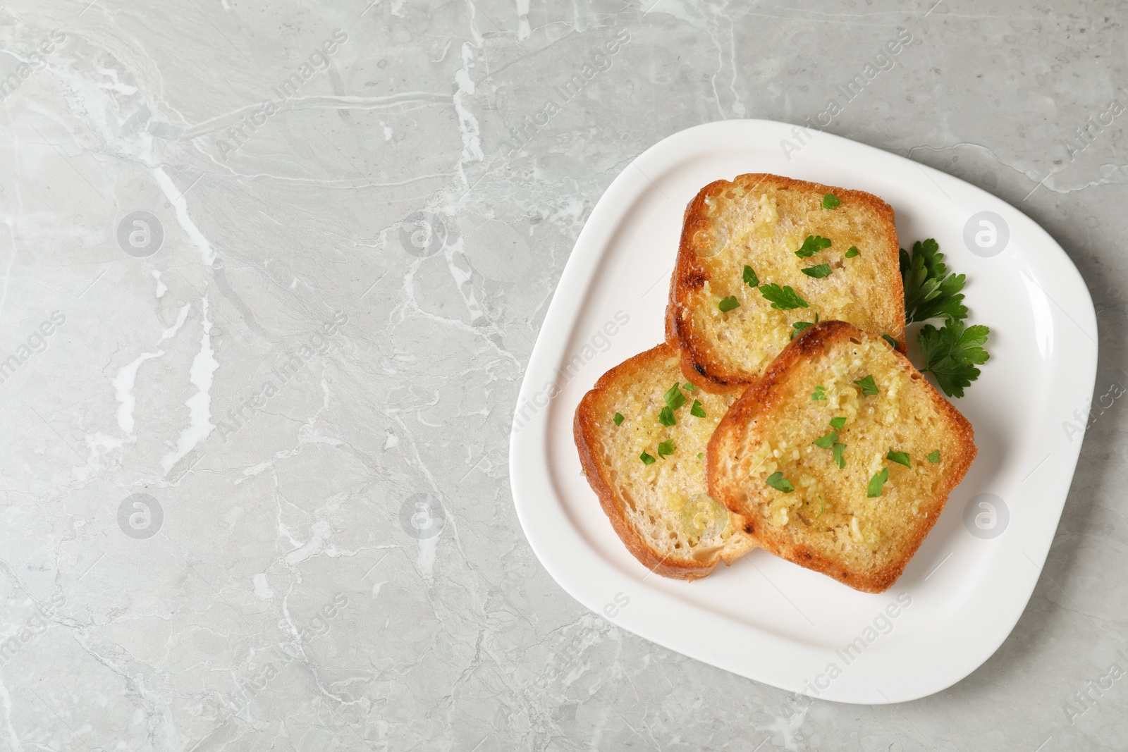 Photo of Slices of toasted bread with garlic and herb on light grey marble table, top view. Space for text