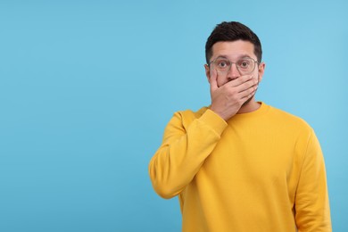 Embarrassed man covering mouth on light blue background. Space for text