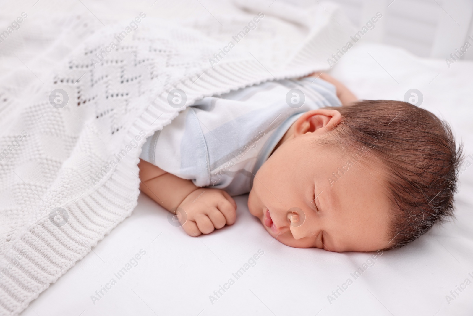 Photo of Cute newborn baby sleeping under white plaid in crib