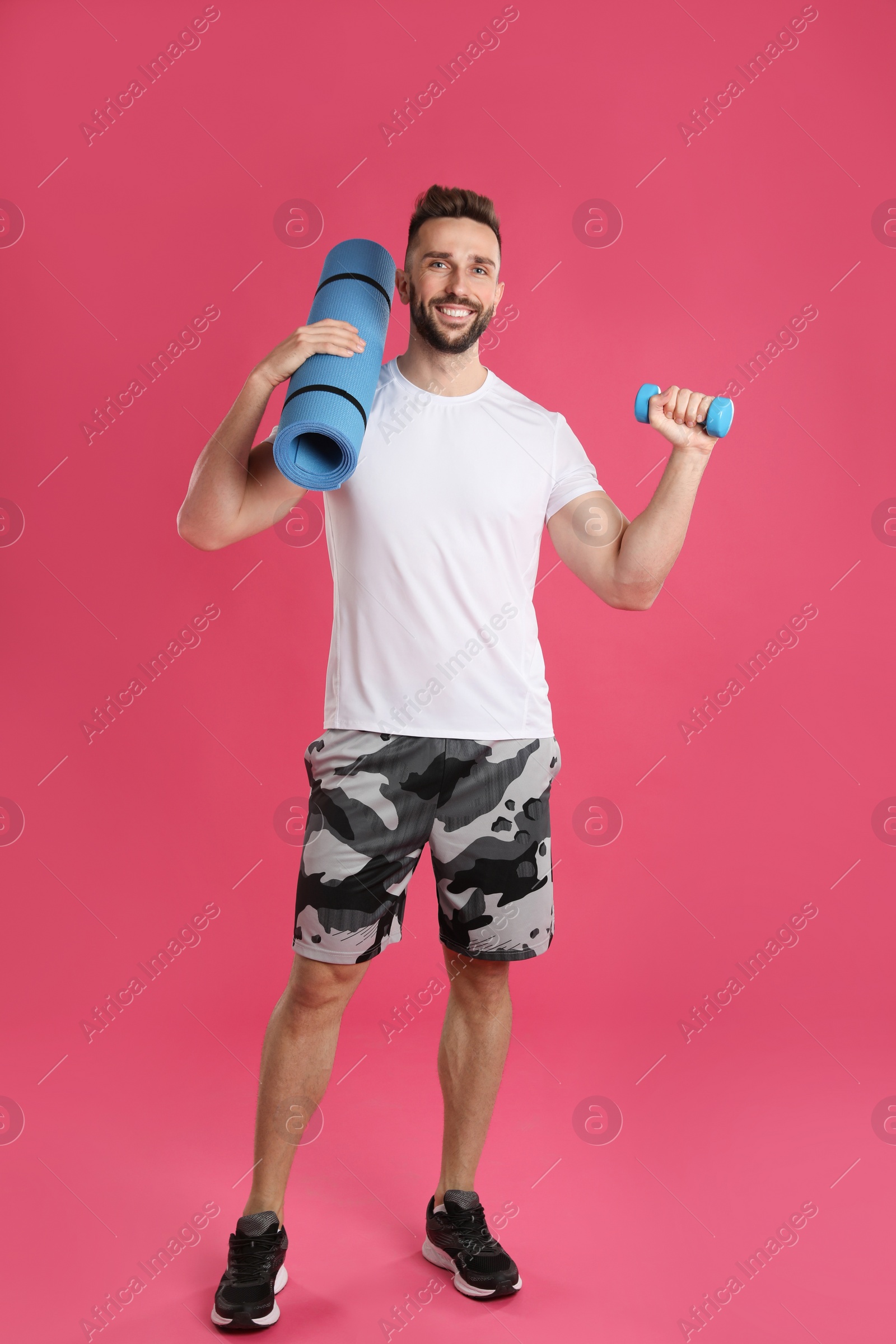 Photo of Handsome man with yoga mat and dumbbell on pink background