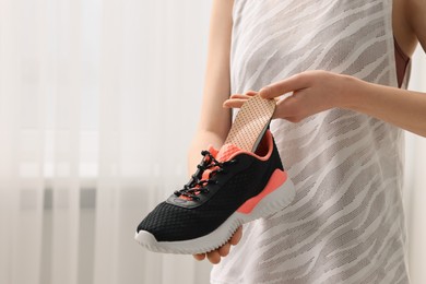 Photo of Woman putting orthopedic insole into shoe indoors, closeup and space for text. Foot care