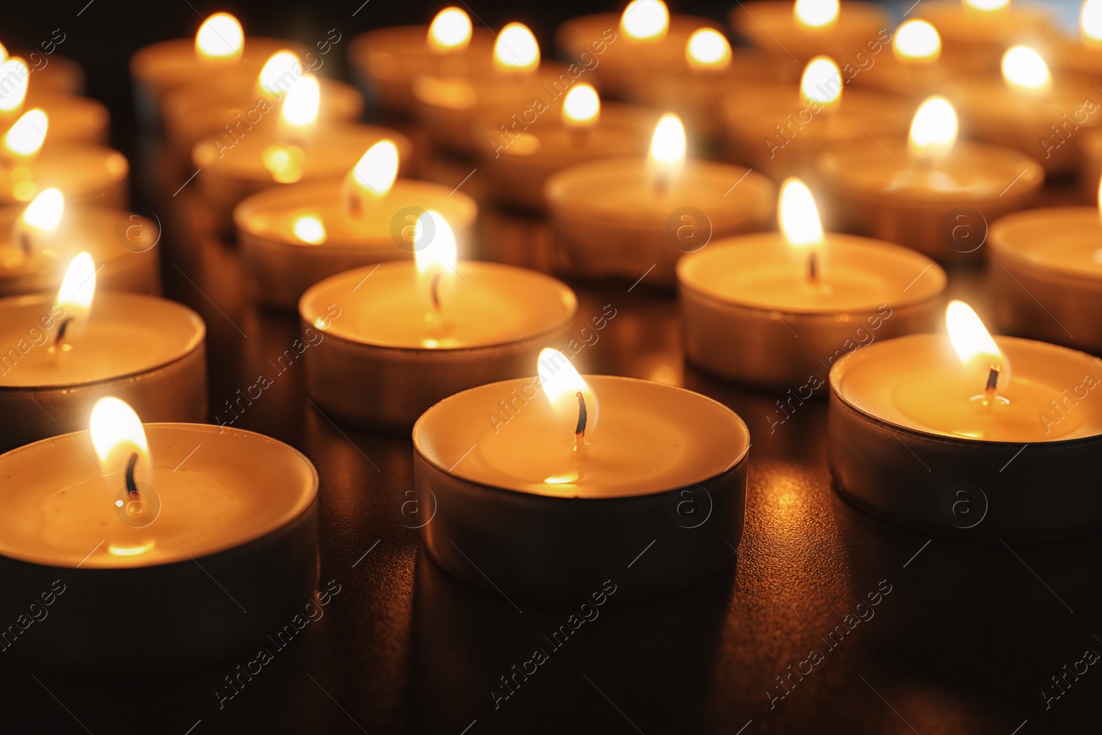 Photo of Wax candles burning on table in darkness, closeup