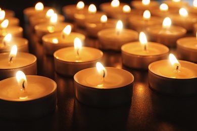 Wax candles burning on table in darkness, closeup