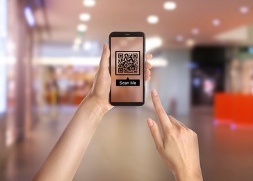 Image of Woman holding smartphone with QR code on screen in shopping mall, closeup