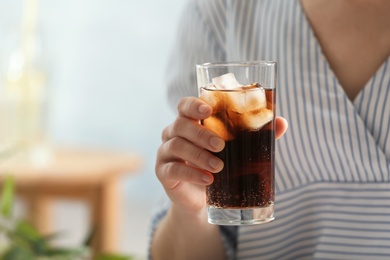 Photo of Woman with glass of cold cola at table indoors, closeup. Space for text
