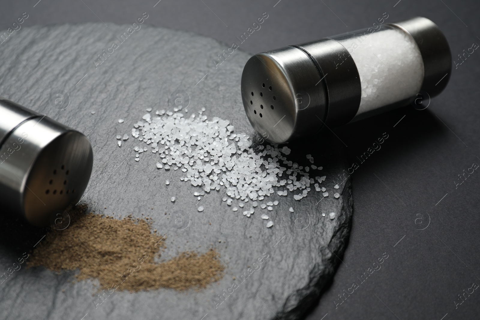 Photo of Salt and pepper shakers on dark table, closeup