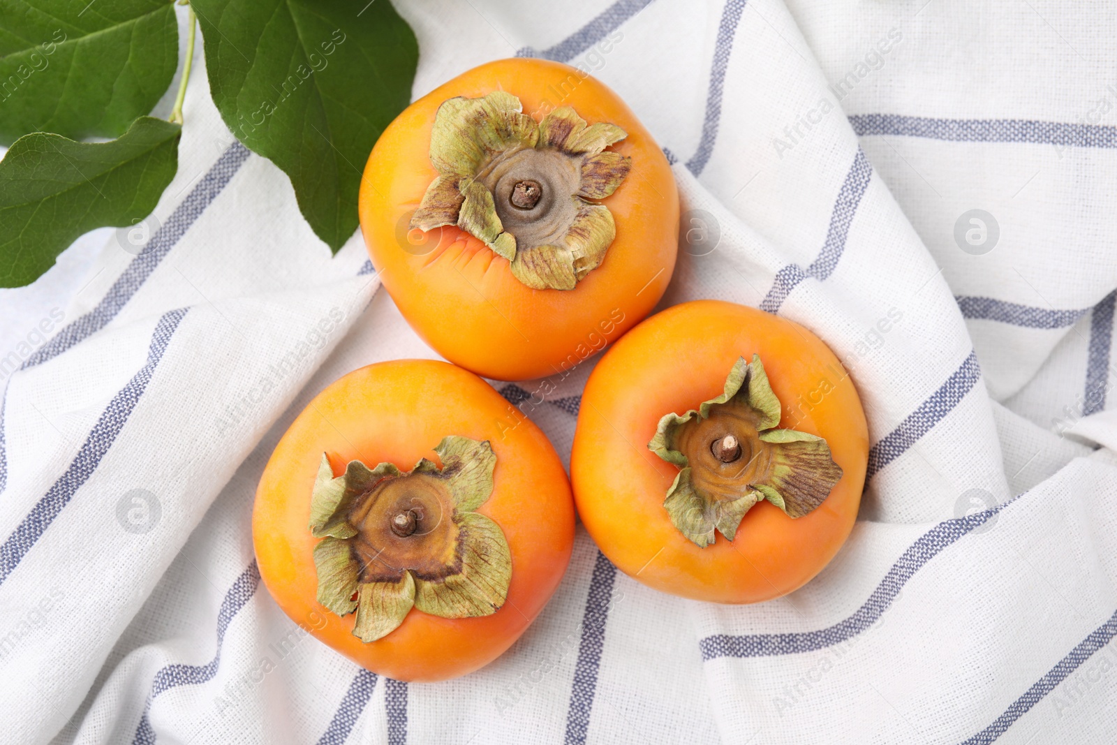 Photo of Delicious ripe juicy persimmons on striped cloth, flat lay