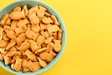 Photo of Delicious goldfish crackers in bowl on yellow background, top view. Space for text