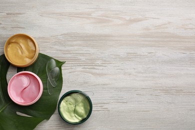 Photo of Packages of different under eye patches and tropical leaf on wooden table, flat lay with space for text. Cosmetic product