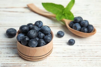Photo of Wooden bowl and spoon of tasty blueberries on white table