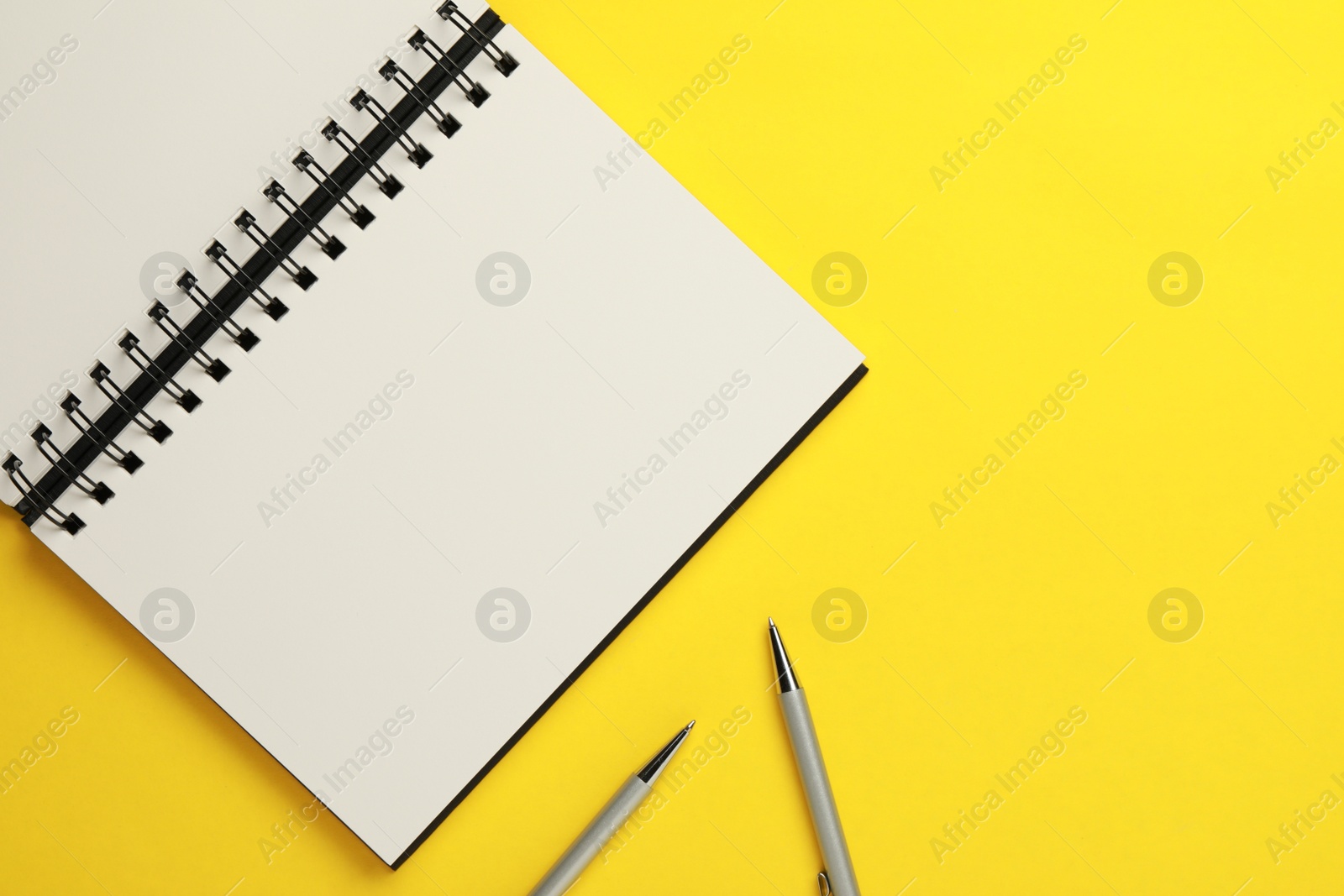 Photo of Notebook and pens on yellow background, flat lay. Space for text