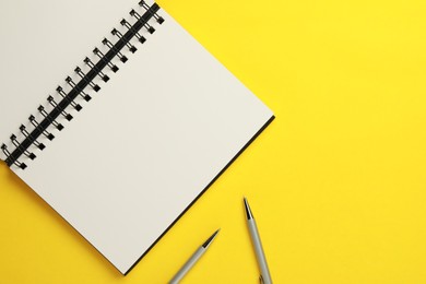 Photo of Notebook and pens on yellow background, flat lay. Space for text