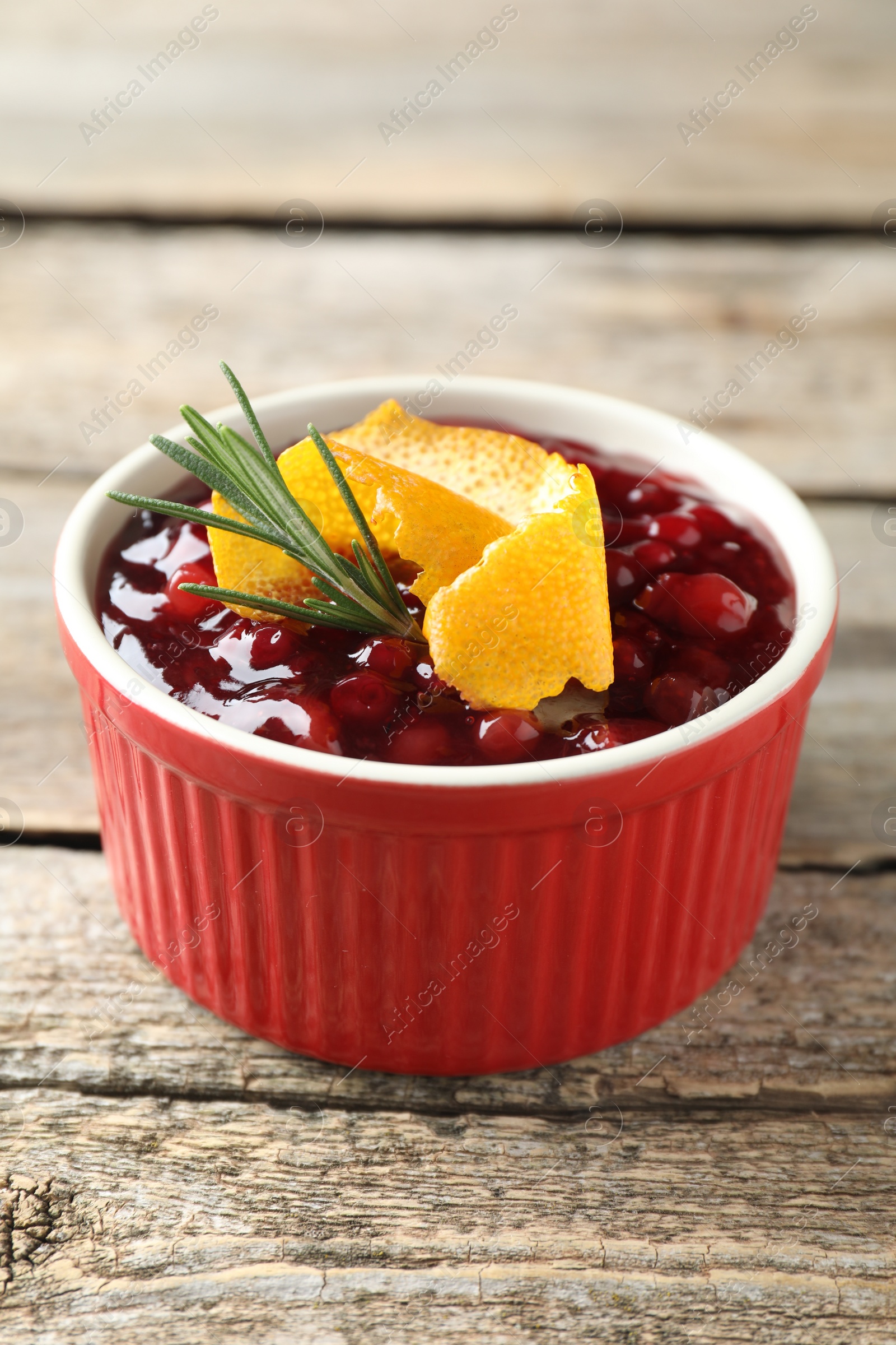 Photo of Fresh cranberry sauce in bowl, rosemary and orange peel on wooden table, closeup