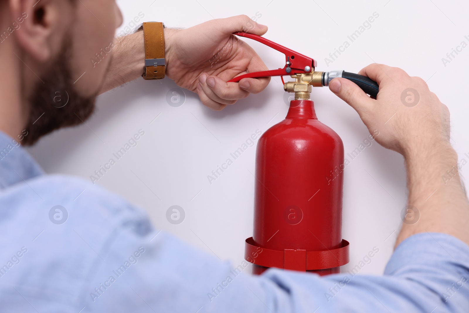 Photo of Man checking quality of fire extinguisher indoors, closeup