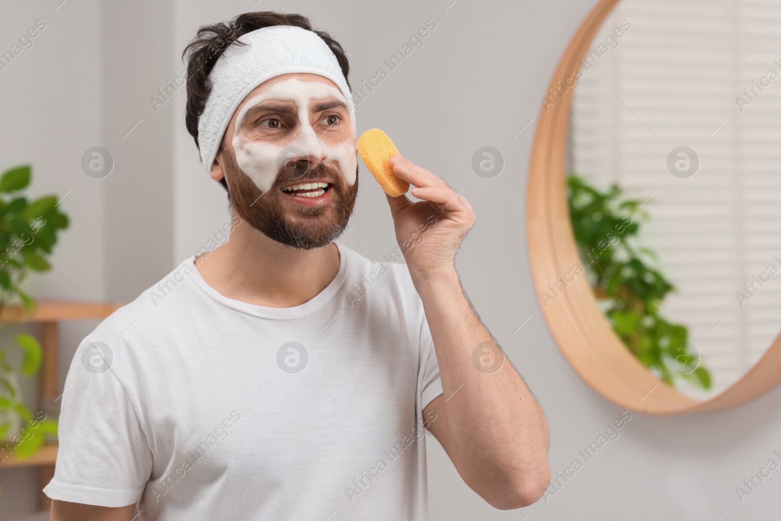 Photo of Man with headband washing his face using sponge in bathroom, space for text