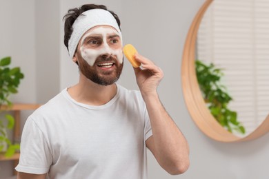 Photo of Man with headband washing his face using sponge in bathroom, space for text