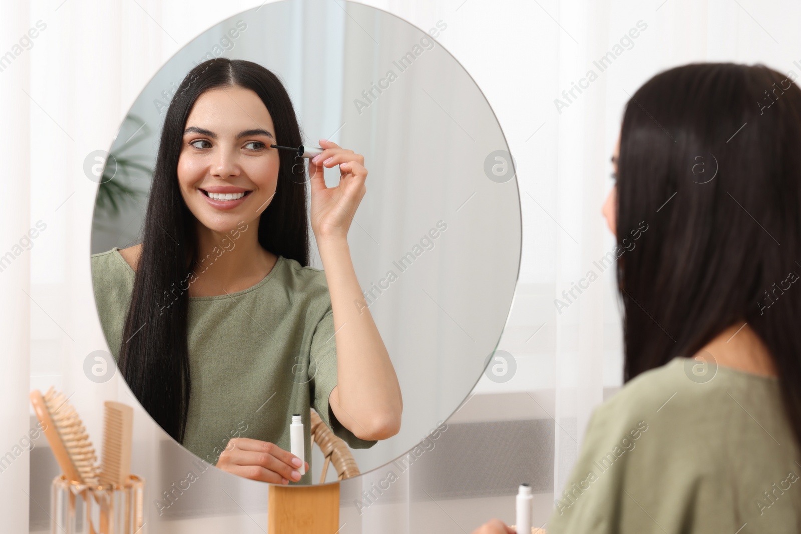 Photo of Beautiful woman applying serum onto her eyelashes in room. Cosmetic product