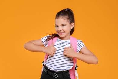 Photo of Cute schoolgirl showing thumbs up on orange background