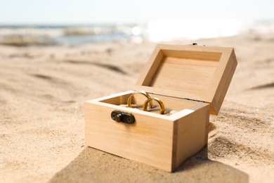 Photo of Beautiful wooden box with gold wedding rings on sandy beach