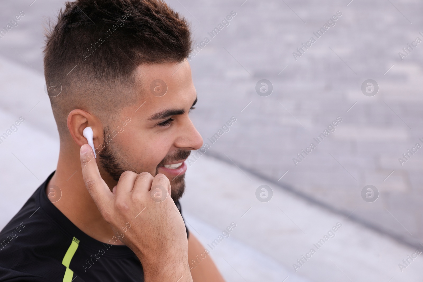 Photo of Young man with wireless headphones listening to music on stairs. Space for text