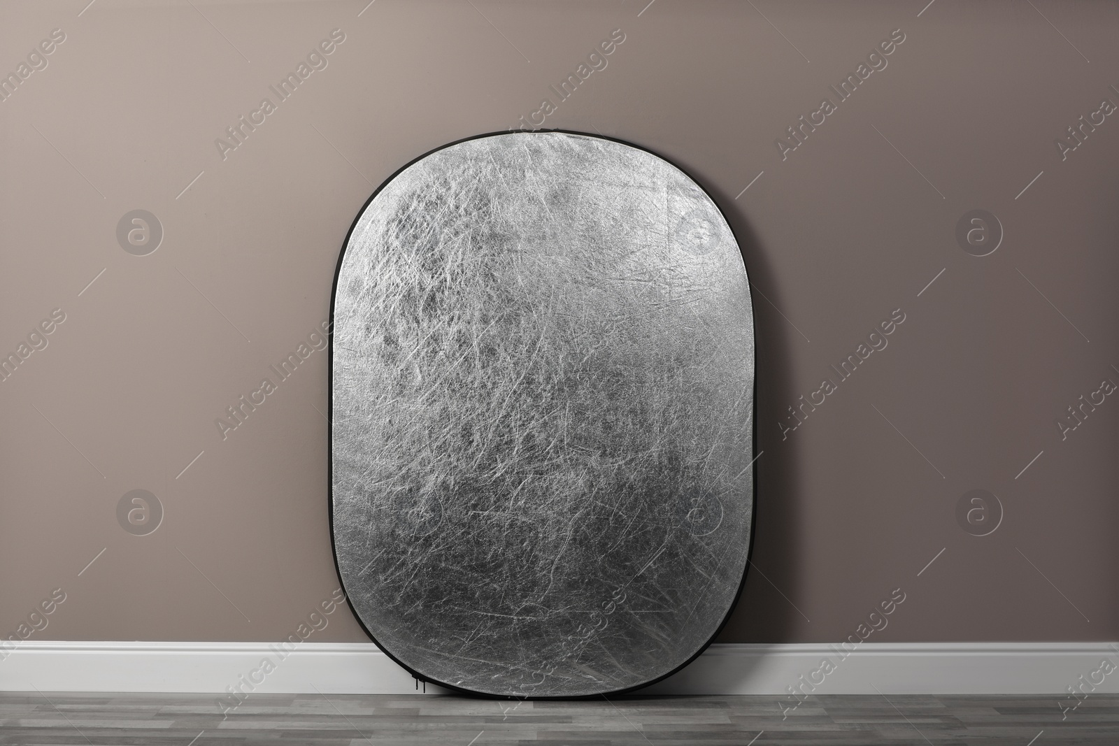Photo of Professional silver reflector near grey wall in room. Photography equipment