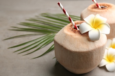Fresh coconut with drinking straw and flowers on grey table, closeup. Space for text