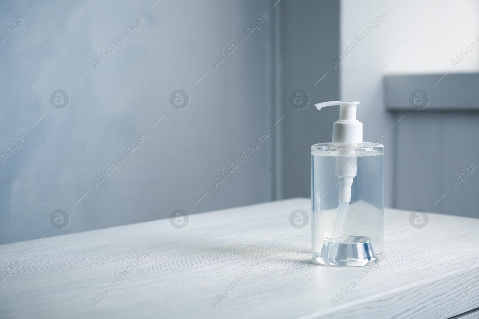 Photo of Dispenser bottle with antiseptic gel on table indoors. Space for text