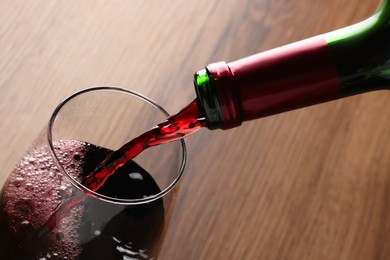 Pouring tasty red wine in glass at wooden table, closeup