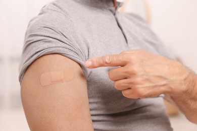 Photo of Man pointing at adhesive bandage after vaccination against blurred background, closeup