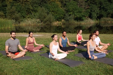 Group of people practicing yoga on mats outdoors. Lotus pose