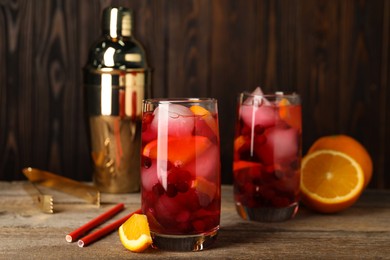 Tasty cranberry cocktail with ice cubes and orange in glasses on wooden table