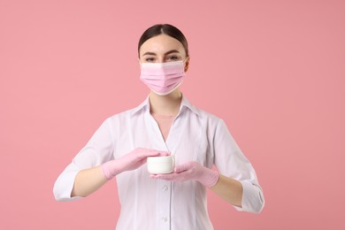 Cosmetologist with cosmetic product on pink background