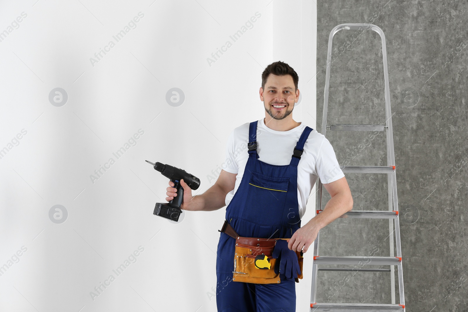 Photo of Handsome working man with electric screwdriver near wall. Home repair