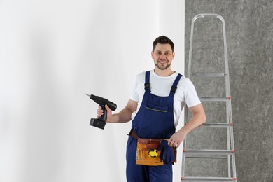 Handsome working man with electric screwdriver near wall. Home repair