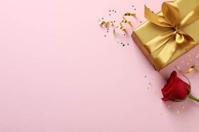 Golden gift box, red rose, confetti and streamers on pink background, flat lay. Space for text