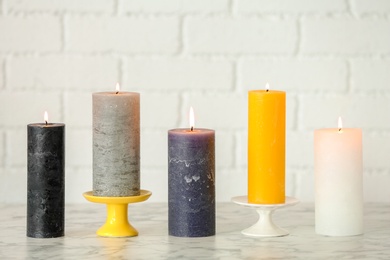 Photo of Different decorative wax candles on table against brick wall