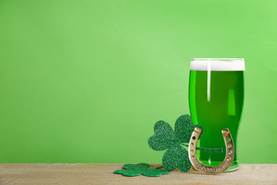 Photo of Green beer, horseshoe and clover leaves on wooden table, space for text. St. Patrick's Day celebration