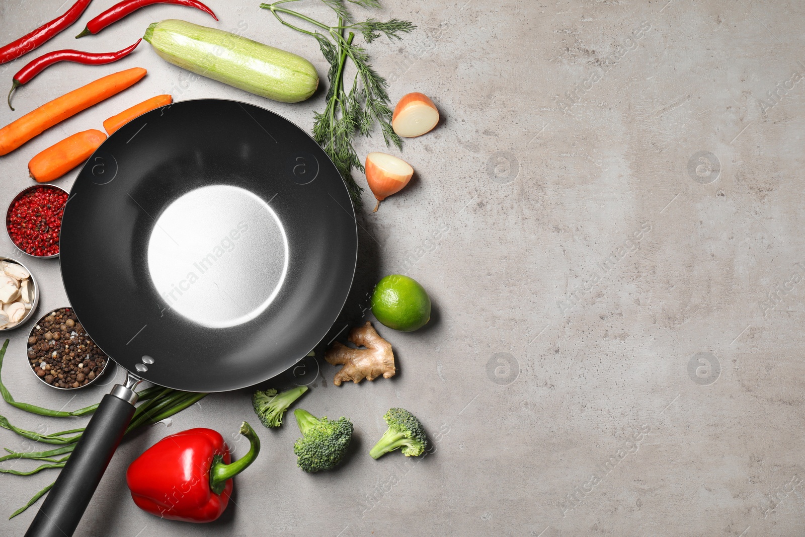 Photo of Empty iron wok surrounded by raw ingredients on grey table, flat lay. Space for text