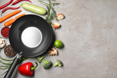 Empty iron wok surrounded by raw ingredients on grey table, flat lay. Space for text