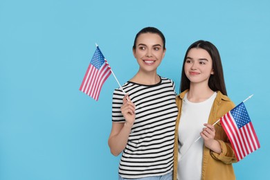 4th of July - Independence Day of USA. Happy woman and her daughter with American flags on light blue background, space for text