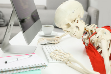 Photo of Human skeleton in red dress using computer at table
