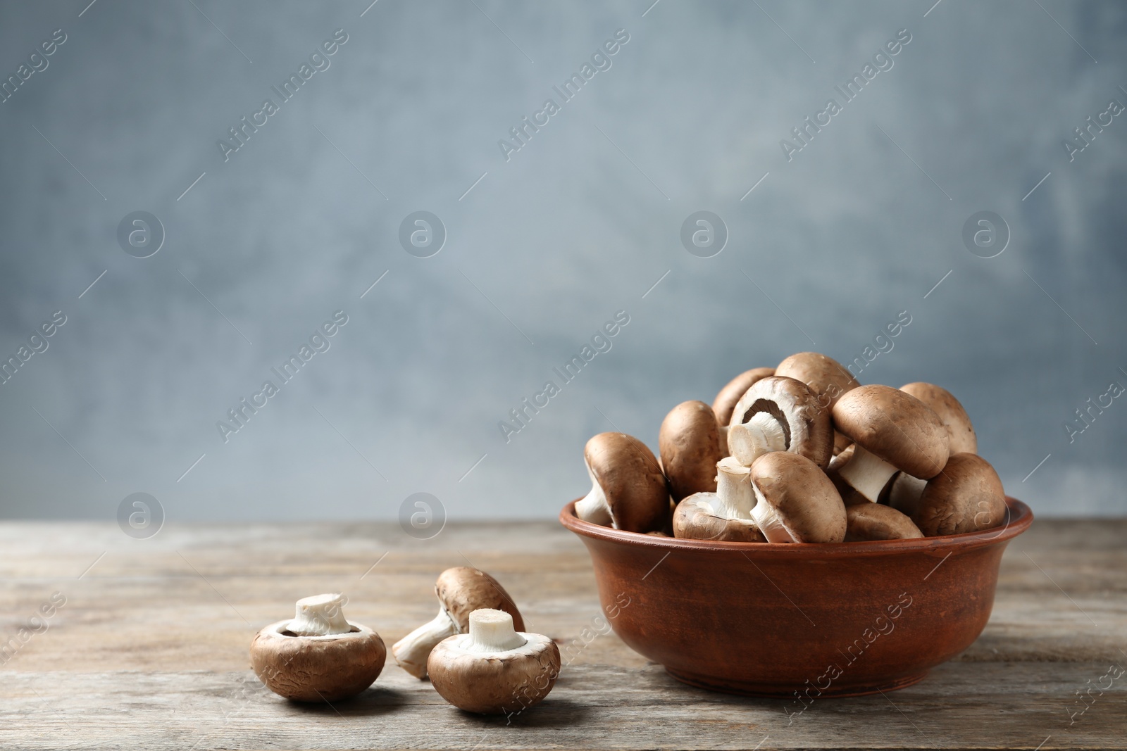 Photo of Fresh champignon mushrooms and bowl on wooden table, space for text