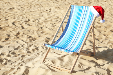 Photo of Deck chair with Santa Claus hat on sandy beach. Christmas vacation