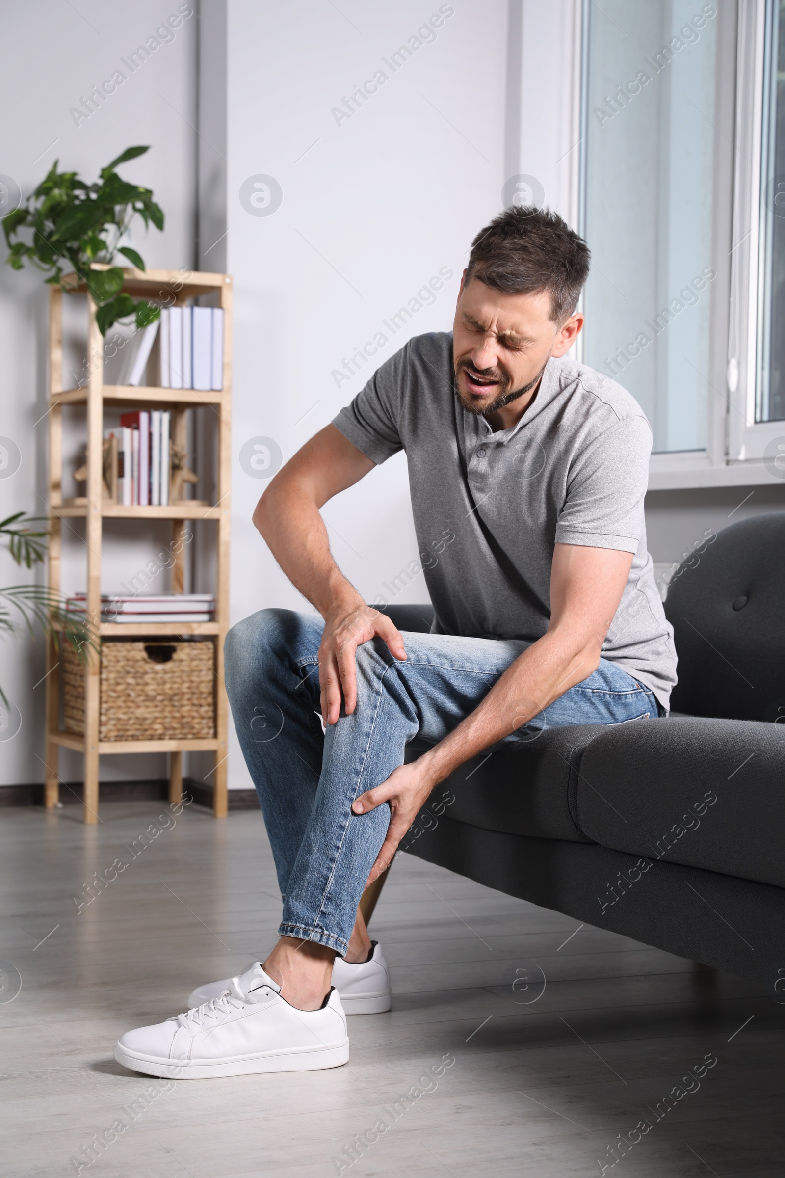 Photo of Man suffering from knee pain on sofa at home