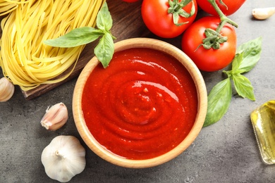 Photo of Flat lay composition with bowl of tasty tomato sauce on grey table